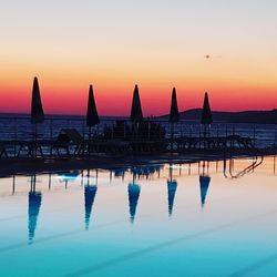 Silhouette swimming pool by sea against sky during sunset