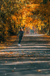 Young girl sits on a skateboard.aerial view of road in autumn with colorful trees.