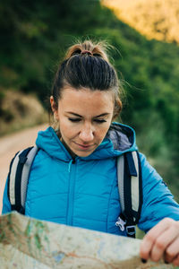Female hiker in warm clothes standing in nature and orientating with paper map during trekking
