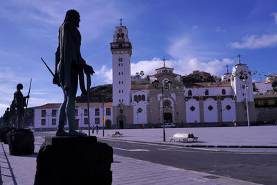 Statue by street and buildings against sky in city