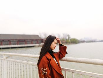 Side view of young woman with eyes closed standing by railing against lake