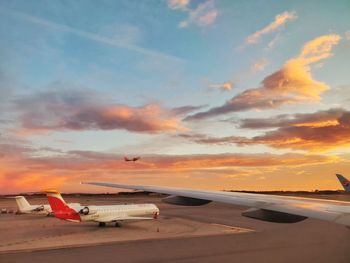 Airplane on airport runway against sky during sunset