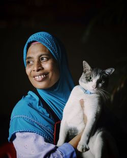 Portrait of smiling young woman with cat against black background