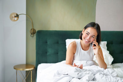 Side view of young woman sitting on bed at home