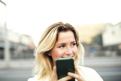 Happy young woman using mobile phone in city against clear sky