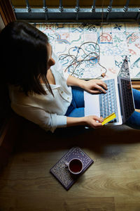 Top view of young woman shopping and paying online on a laptop with credit card while relaxing at home next to a window.