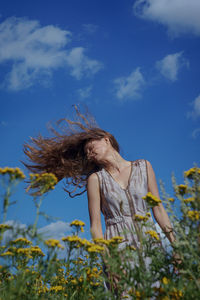 Low angle view of woman tossing hair while standing at field