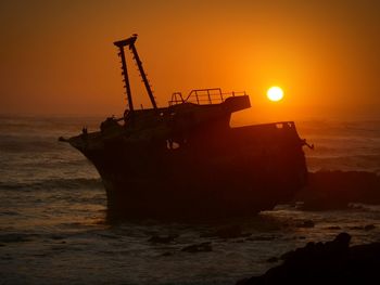 Silhouette boat on beach against sky during sunset