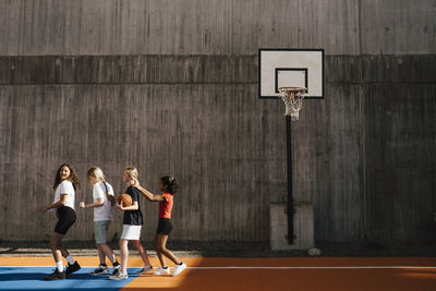 Female friends walking in a row by wall at basketball court