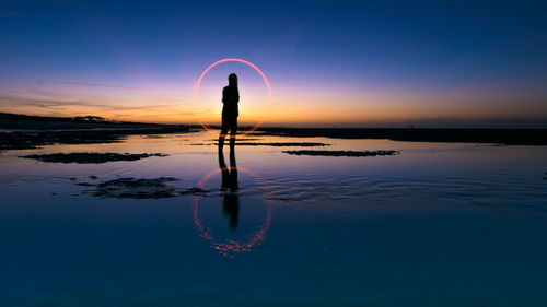 Silhouette person spinning wire wool at wet beach