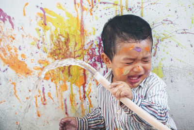 Crying boy holding garden hose while painting wall 