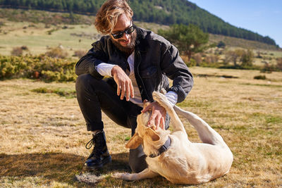 Portrait of young tattoed man playing with his dog in the countryside