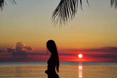 Silhouette woman looking at sea against sky during sunset