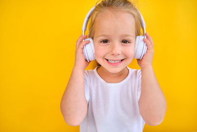 Portrait of young woman holding headphones while standing against yellow background