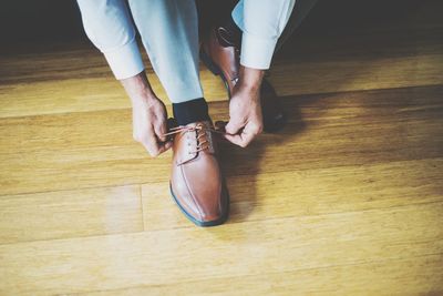 Low section of man tying shoelace on hardwood floor