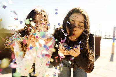 Young women blowing confetti during sunny day