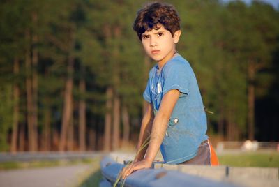 Serious boy leaning on fence on field