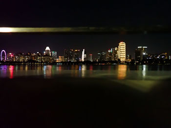 Illuminated buildings by river against sky at night