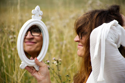 Smiling woman holding mirror while standing on field