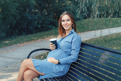 Portrait of smiling woman holding disposable cup while sitting on seat