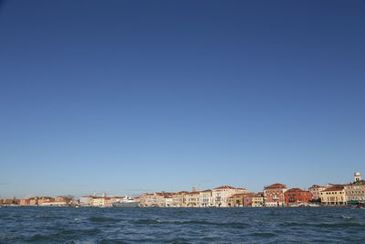 Buildings by sea against clear blue sky