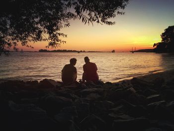 Silhouette people sitting on beach against sky during sunset