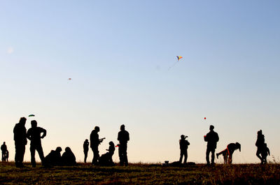 People flying kites on field against sky