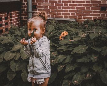 Girl holding plant while standing against brick wall