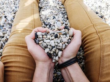 Cropped image of man holding pebbles while sitting at beach