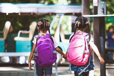Rear view of schoolgirls carrying backpacks while walking on street