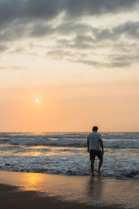 Rear view of woman walking at beach against sky during sunset