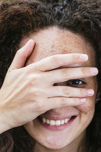 Smiling young woman covering eye with hand
