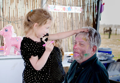 A little girl looks at her art work as she is putting makeup on grandpa