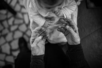 Low section of senior woman hands reaching towards toddler on footpath