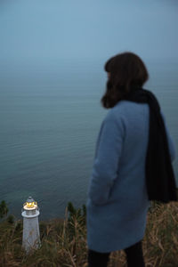 Rear view of woman standing by sea against sky