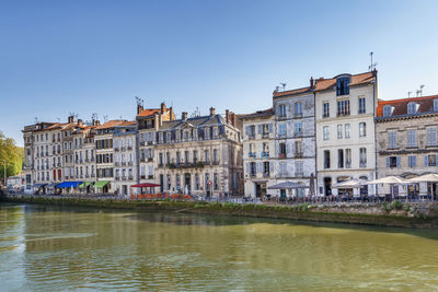 Buildings by river in city against clear sky