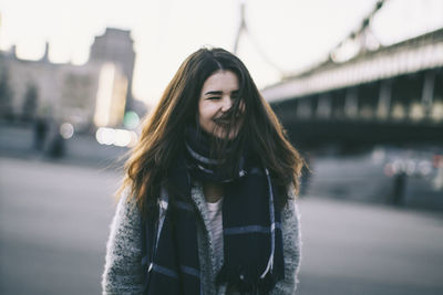 Cheerful young woman wearing scarf standing on street during winter