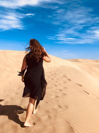 Rear view of woman walking on sand dune