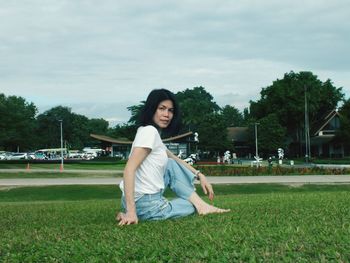 Portrait of smiling woman sitting on grass against sky