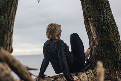 Rear view of woman sitting on tree trunk against sky