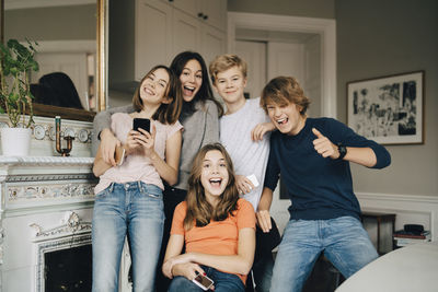 Portrait of cheerful friends with mobile phones in living room at home