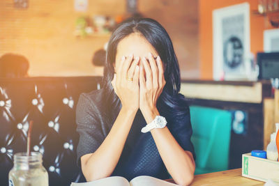 Woman covering face with hands while sitting in cafe