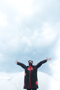 Man with arms outstretched standing against cloudy sky