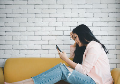 Young woman using mobile phone while sitting on wall