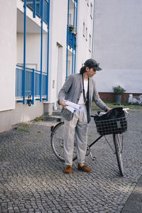 Full length of male architect holding blueprint rolls standing by bicycle on footpath