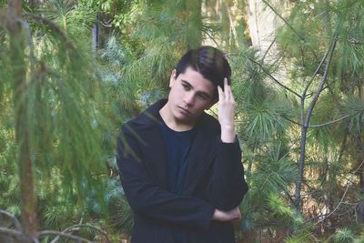 Young man standing by plants against trees