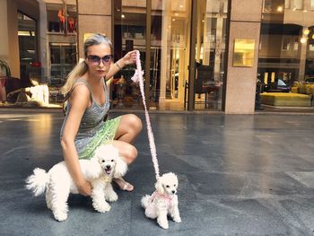 Portrait of mature woman wearing sunglasses with dogs crouching on footpath against building in city