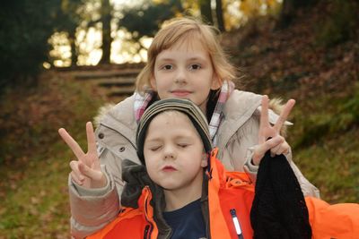 Siblings gesturing peace sign at park during sunset