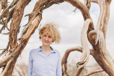 Young woman standing by bare tree against sky