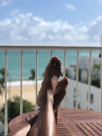 Low section of person resting on table by railing against sea and sky